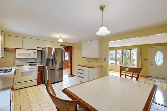 kitchen with a wealth of natural light, backsplash, white appliances, and pendant lighting