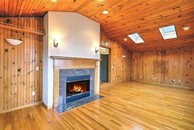 unfurnished living room featuring lofted ceiling with skylight, wood finished floors, a high end fireplace, wooden ceiling, and wood walls