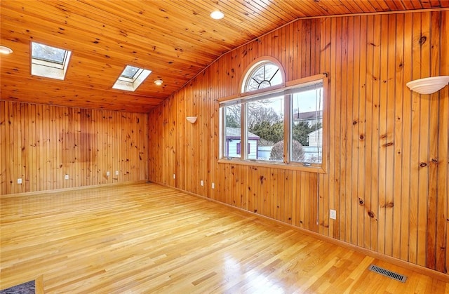 empty room with visible vents, lofted ceiling with skylight, wood walls, wooden ceiling, and wood finished floors