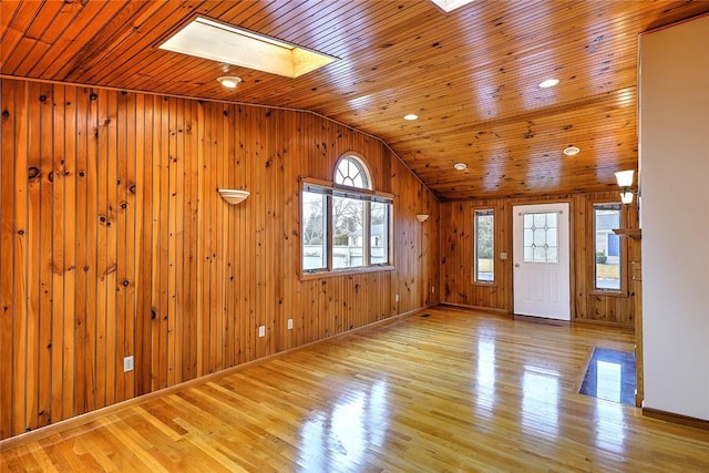 entrance foyer with baseboards, lofted ceiling with skylight, wood walls, wood ceiling, and wood finished floors