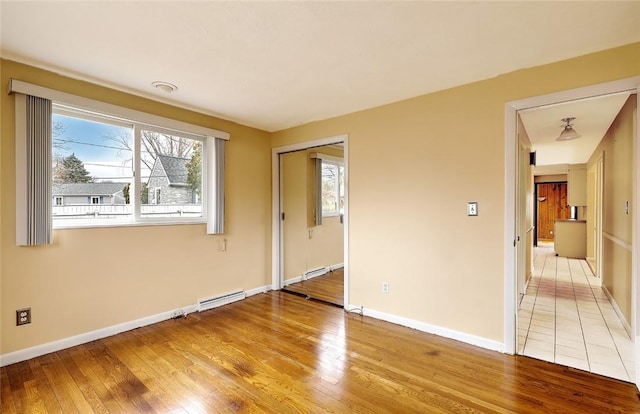 unfurnished room featuring plenty of natural light, baseboards, light wood-style floors, and a baseboard radiator