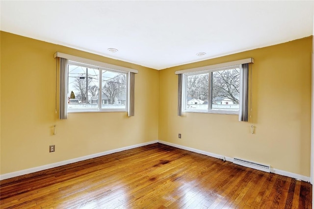 unfurnished room featuring a baseboard heating unit, wood-type flooring, and baseboards