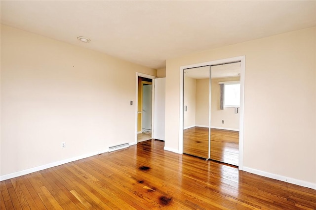 unfurnished bedroom featuring a baseboard heating unit, a closet, baseboards, and wood-type flooring