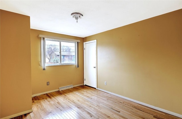 spare room featuring baseboard heating, light wood-style flooring, and baseboards