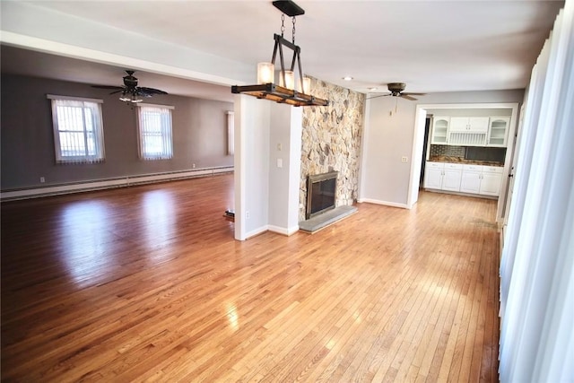 unfurnished living room with a baseboard heating unit, a stone fireplace, a ceiling fan, and hardwood / wood-style floors