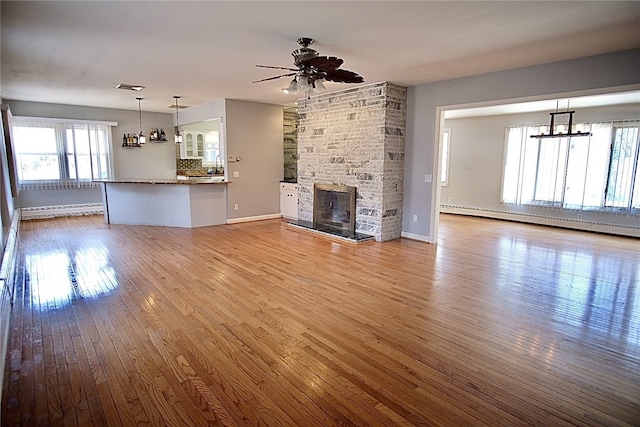 unfurnished living room with a multi sided fireplace, ceiling fan with notable chandelier, a baseboard radiator, and wood-type flooring