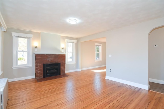 unfurnished living room with light wood-type flooring, baseboards, radiator, and a fireplace