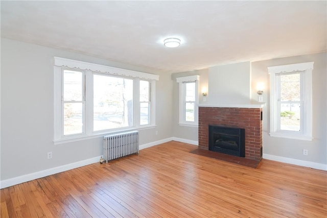 unfurnished living room with radiator heating unit, a fireplace, light wood-type flooring, and baseboards