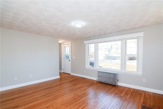 spare room with a wealth of natural light, radiator, baseboards, and light wood-style floors