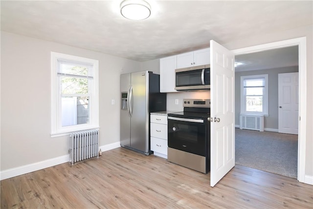 kitchen with baseboards, radiator heating unit, white cabinets, appliances with stainless steel finishes, and light wood-type flooring