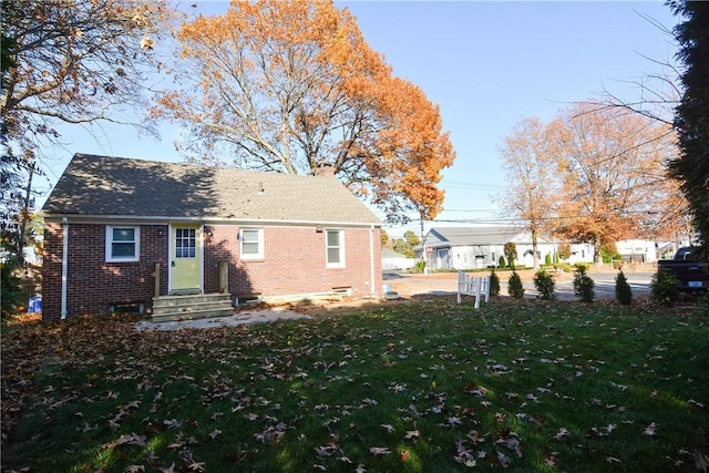 back of house with a yard, brick siding, and a chimney