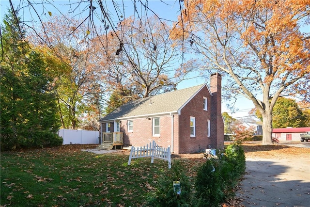 rear view of property featuring a yard, fence, brick siding, and a chimney