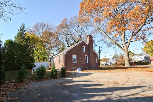 view of side of property featuring fence, brick siding, and a chimney