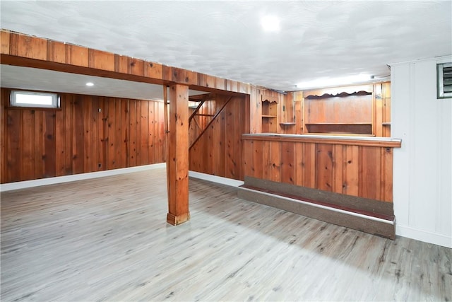 below grade area with wood walls, a bar, baseboards, and wood finished floors