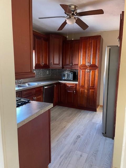 kitchen featuring dishwashing machine, light wood-type flooring, freestanding refrigerator, and a sink