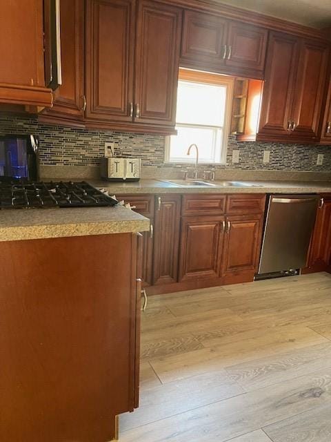 kitchen featuring gas stovetop, a sink, light wood-style floors, dishwasher, and backsplash