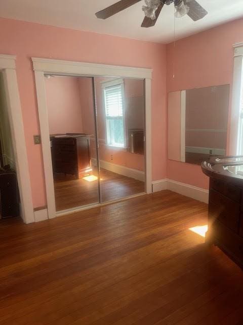 unfurnished bedroom with a closet, baseboards, wood finished floors, and a ceiling fan