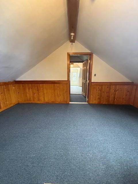 additional living space featuring vaulted ceiling with beams, dark colored carpet, wood walls, and wainscoting