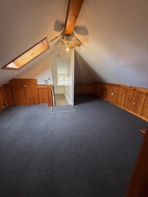 additional living space with lofted ceiling with skylight, wooden walls, and dark colored carpet