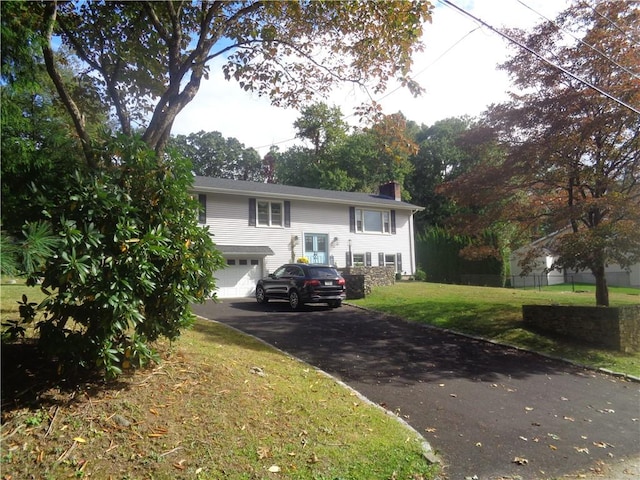 split foyer home with a chimney, driveway, an attached garage, and a front lawn