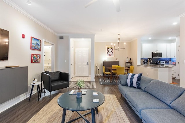 living room with an inviting chandelier, wood finished floors, visible vents, and ornamental molding