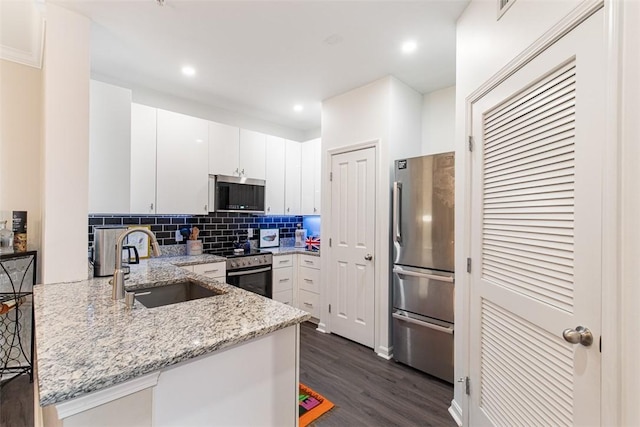 kitchen with a peninsula, a sink, decorative backsplash, dark wood-type flooring, and appliances with stainless steel finishes