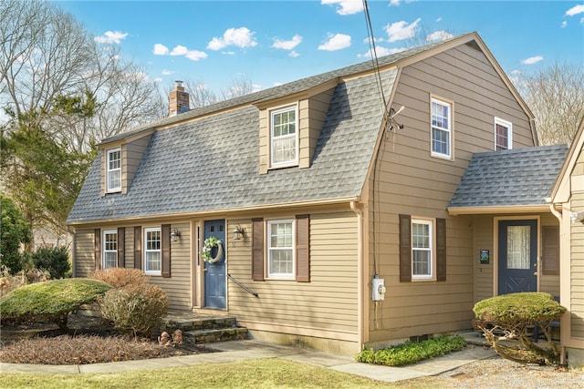 colonial inspired home featuring a gambrel roof, a chimney, and a shingled roof