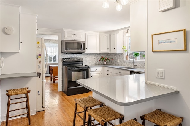 kitchen with a breakfast bar, a peninsula, a sink, black electric range, and stainless steel microwave