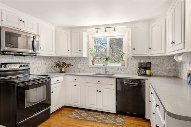 kitchen with white cabinetry, black appliances, light wood-type flooring, and a sink