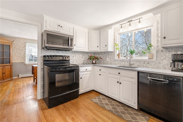 kitchen with a wainscoted wall, black appliances, a sink, wallpapered walls, and baseboard heating