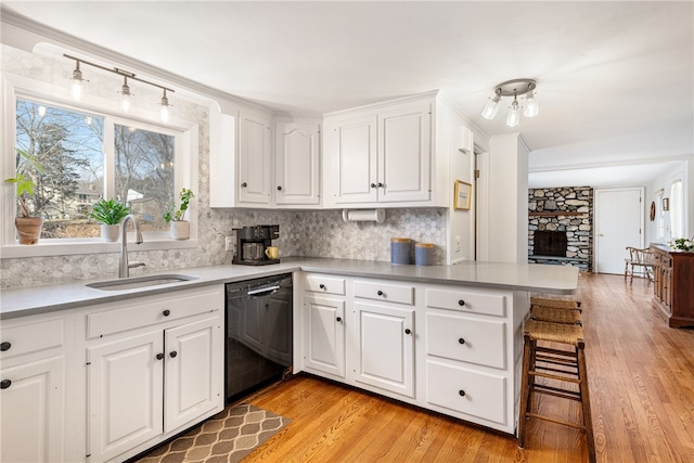 kitchen with light wood-style flooring, a sink, decorative backsplash, white cabinets, and black dishwasher