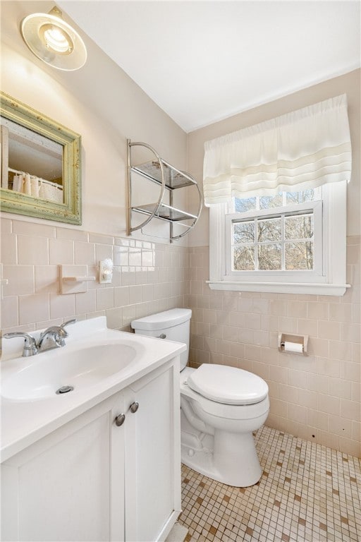 bathroom featuring tile patterned floors, toilet, tile walls, wainscoting, and vanity