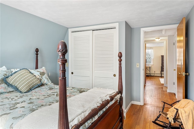 bedroom featuring a closet, baseboard heating, light wood-style flooring, and baseboards