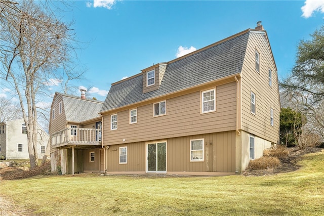 rear view of property with a deck, a yard, roof with shingles, and a chimney