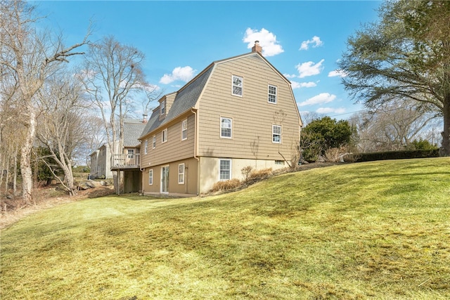 view of home's exterior featuring a deck, a lawn, a chimney, and a gambrel roof