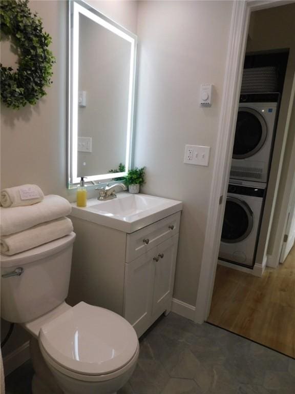 bathroom with vanity, toilet, baseboards, and stacked washing maching and dryer