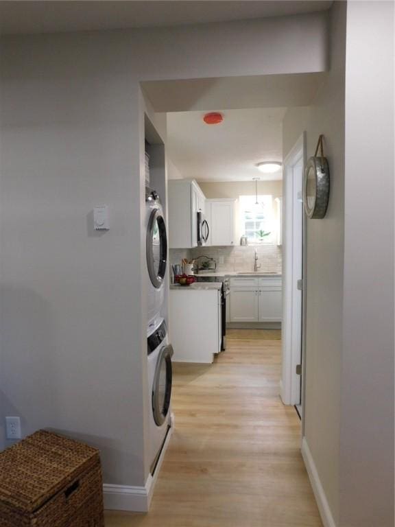 laundry area featuring baseboards, laundry area, a sink, stacked washer and dryer, and light wood-style floors