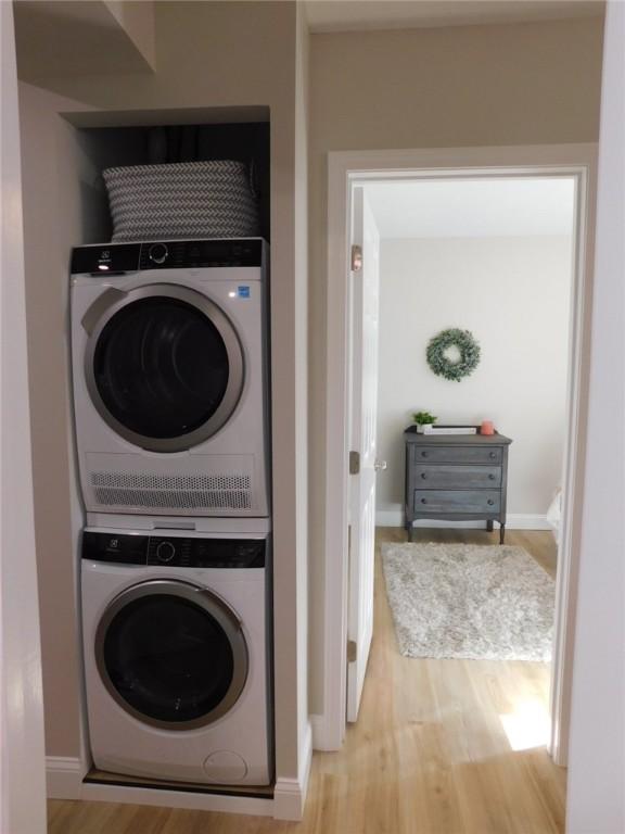 laundry area featuring baseboards, stacked washer and clothes dryer, wood finished floors, and laundry area