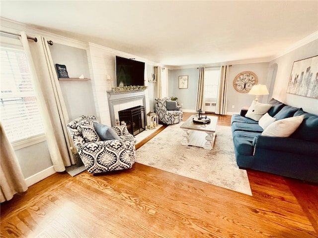 living room featuring a tiled fireplace, wood finished floors, baseboards, and ornamental molding