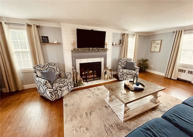 living room with radiator, baseboards, a tiled fireplace, ornamental molding, and wood finished floors