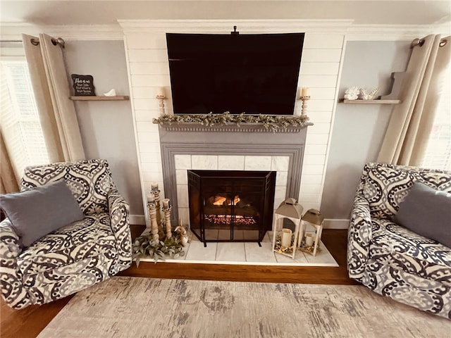 sitting room featuring a tiled fireplace, wood finished floors, a wealth of natural light, and ornamental molding