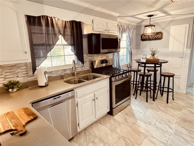 kitchen featuring a wainscoted wall, a sink, ornamental molding, stainless steel appliances, and white cabinetry