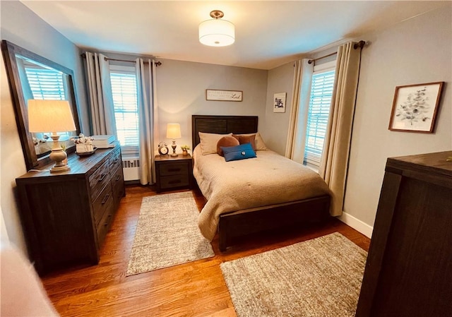 bedroom with multiple windows, radiator, baseboards, and light wood-style floors