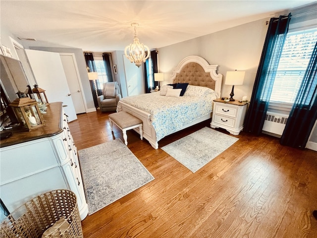 bedroom featuring visible vents, radiator, baseboards, an inviting chandelier, and wood finished floors