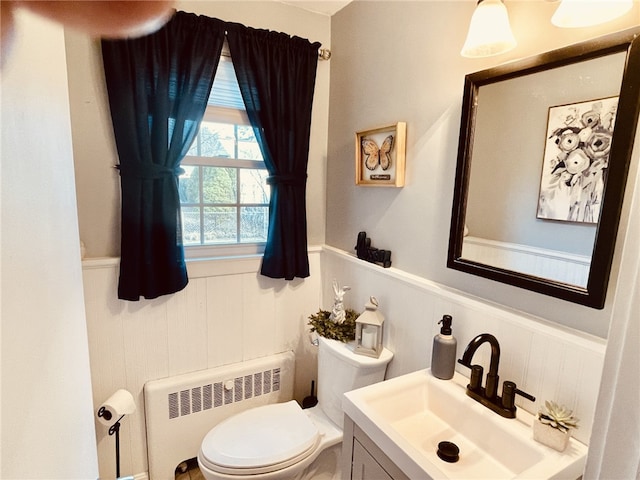 half bathroom featuring a wainscoted wall, radiator, vanity, and toilet