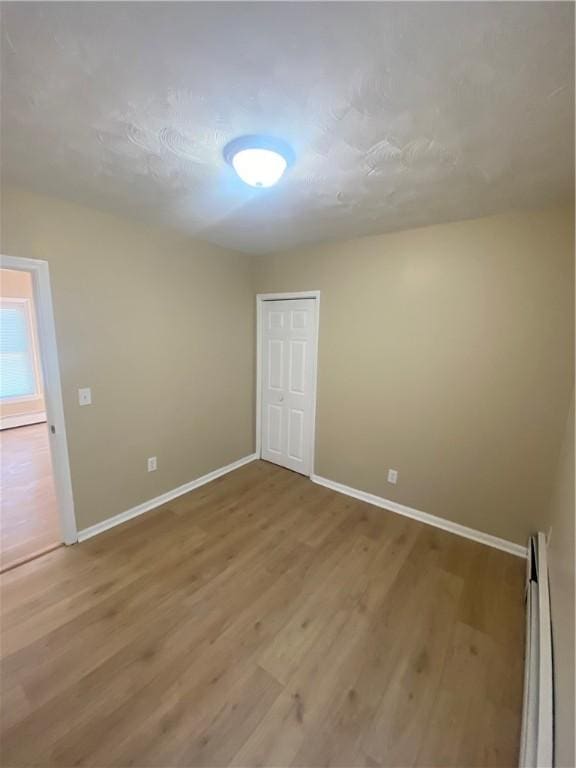 unfurnished bedroom with light wood finished floors, a closet, a baseboard heating unit, and baseboards