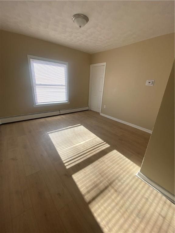 unfurnished room featuring baseboards, baseboard heating, wood finished floors, and a textured ceiling