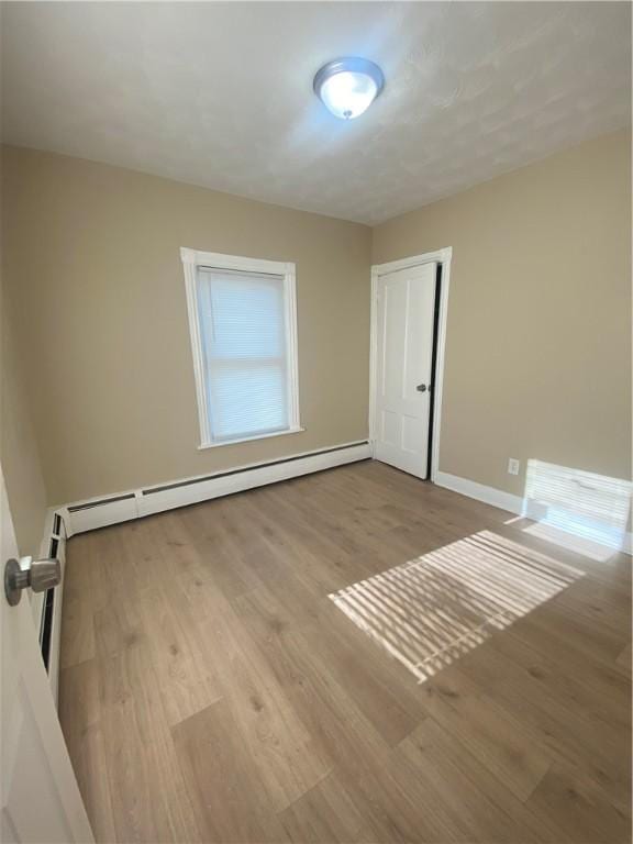 spare room featuring a baseboard heating unit, baseboards, and wood finished floors