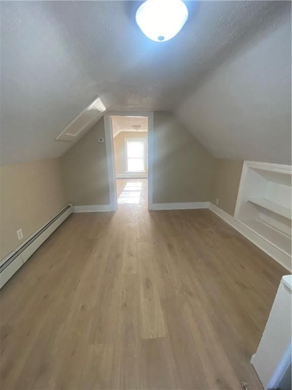 additional living space with a textured ceiling, baseboards, lofted ceiling, and wood finished floors