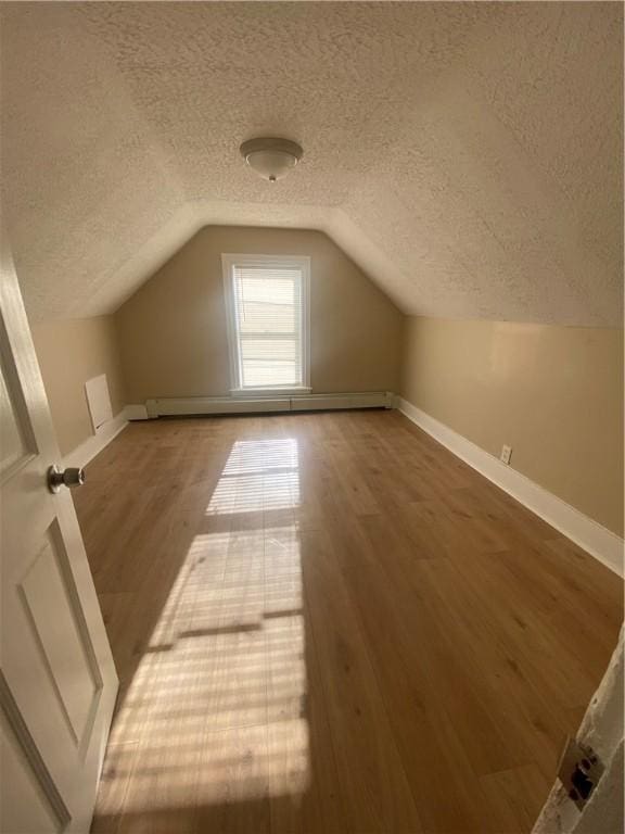 bonus room with baseboards, vaulted ceiling, wood finished floors, a textured ceiling, and a baseboard radiator